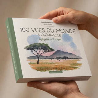 Mains présentant un livre d'aquarelle "100 vues du monde" avec illustration paysage africain sur couverture verte